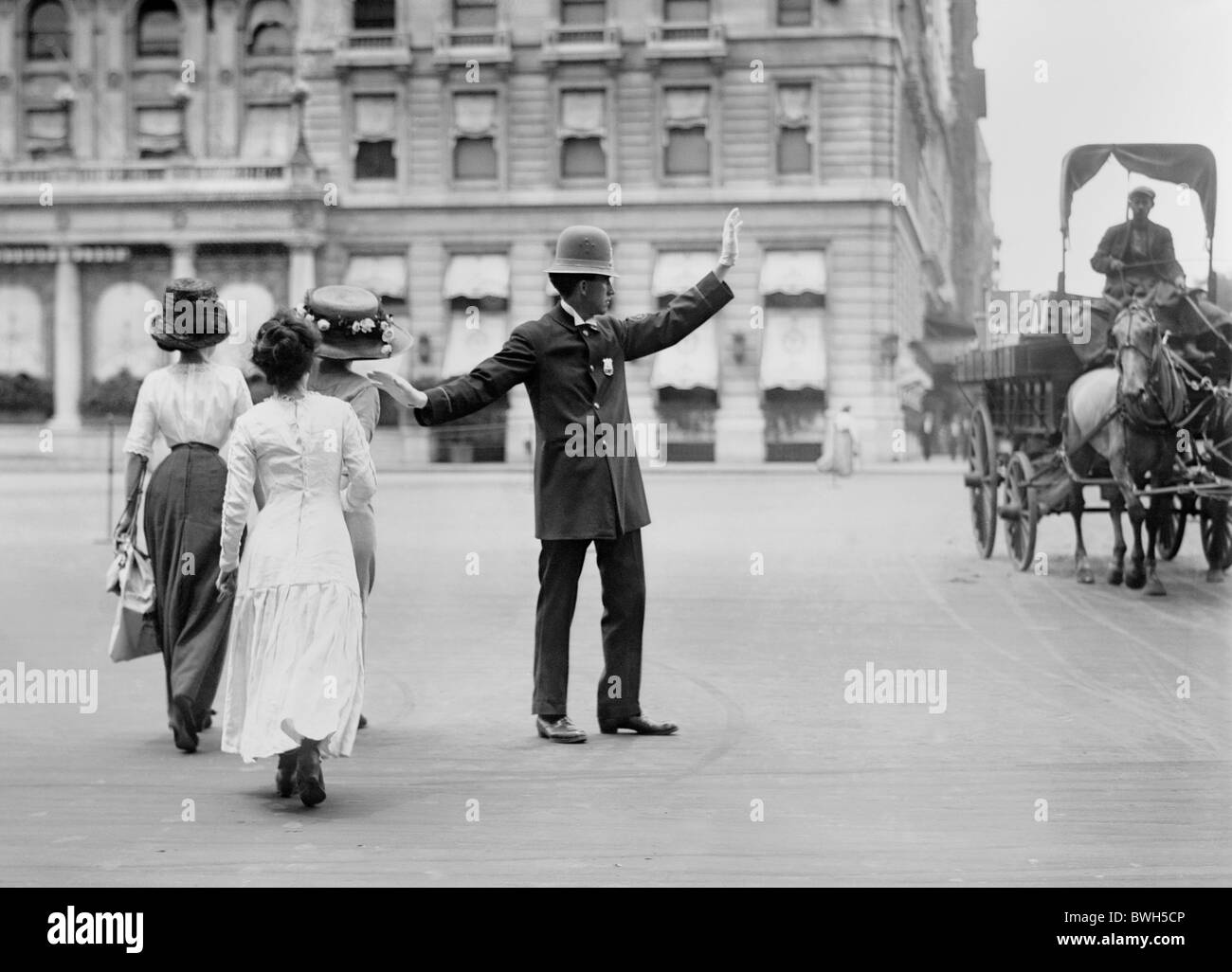 Vintage photo c1911 of a traffic cop in New York City halting a horse-drawn wagon to allow three women to cross the road safely. Stock Photo