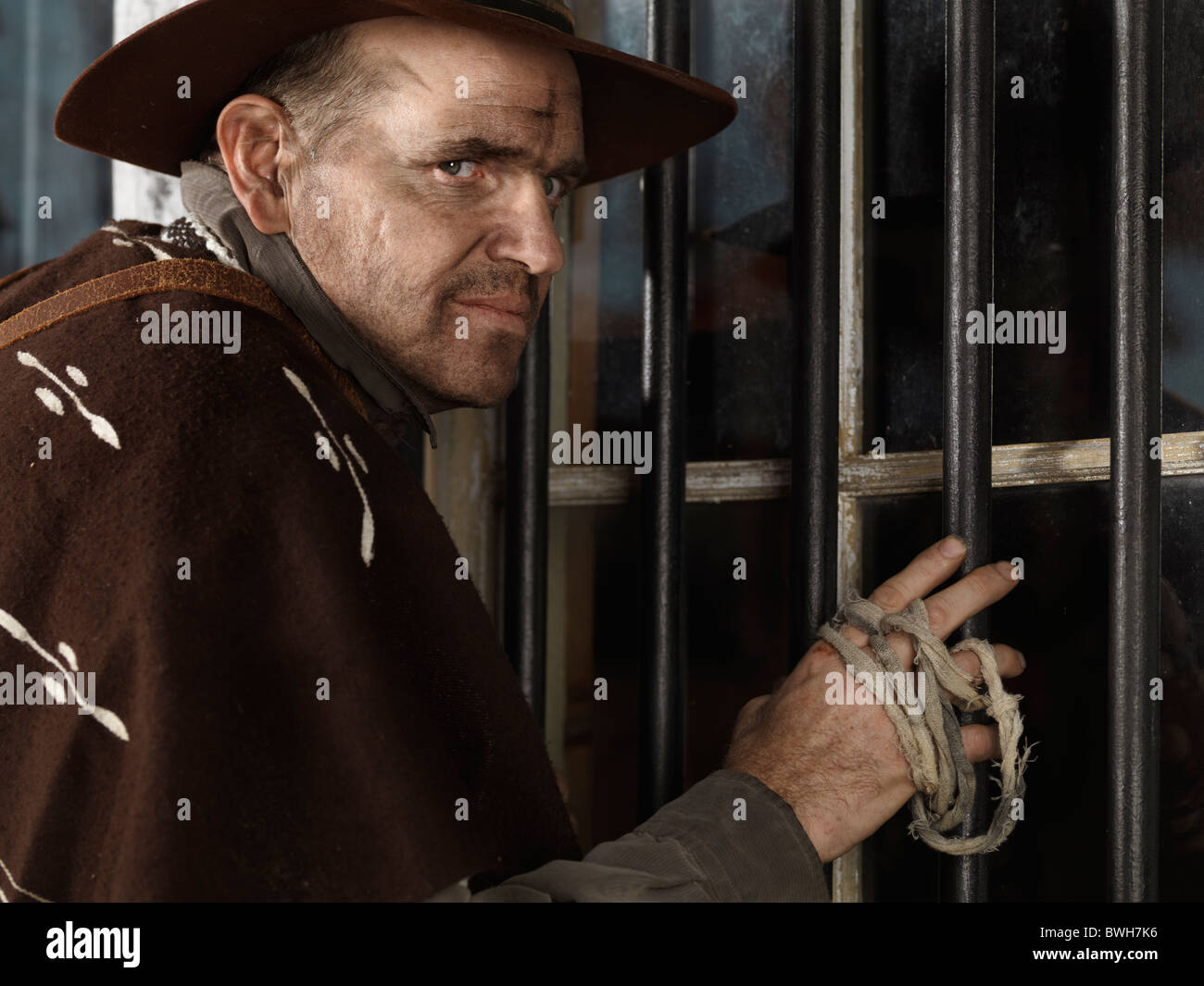 Cowboy standing at a barred window, attempting to rob a bank at night Stock Photo
