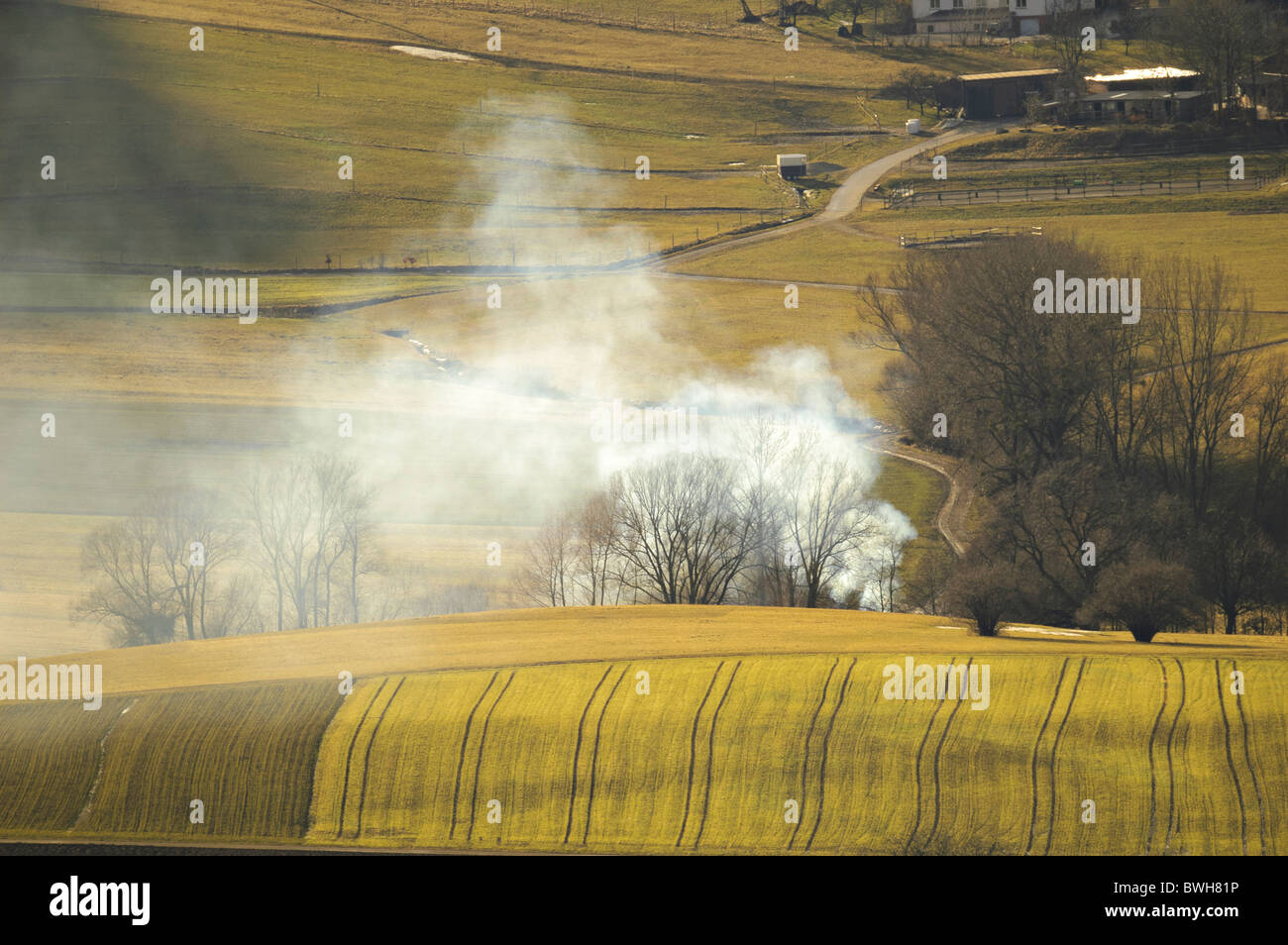 Smoke over agrarian fields sprayed with liquid manure, horse barn in background, Swabian alb, Germany Stock Photo