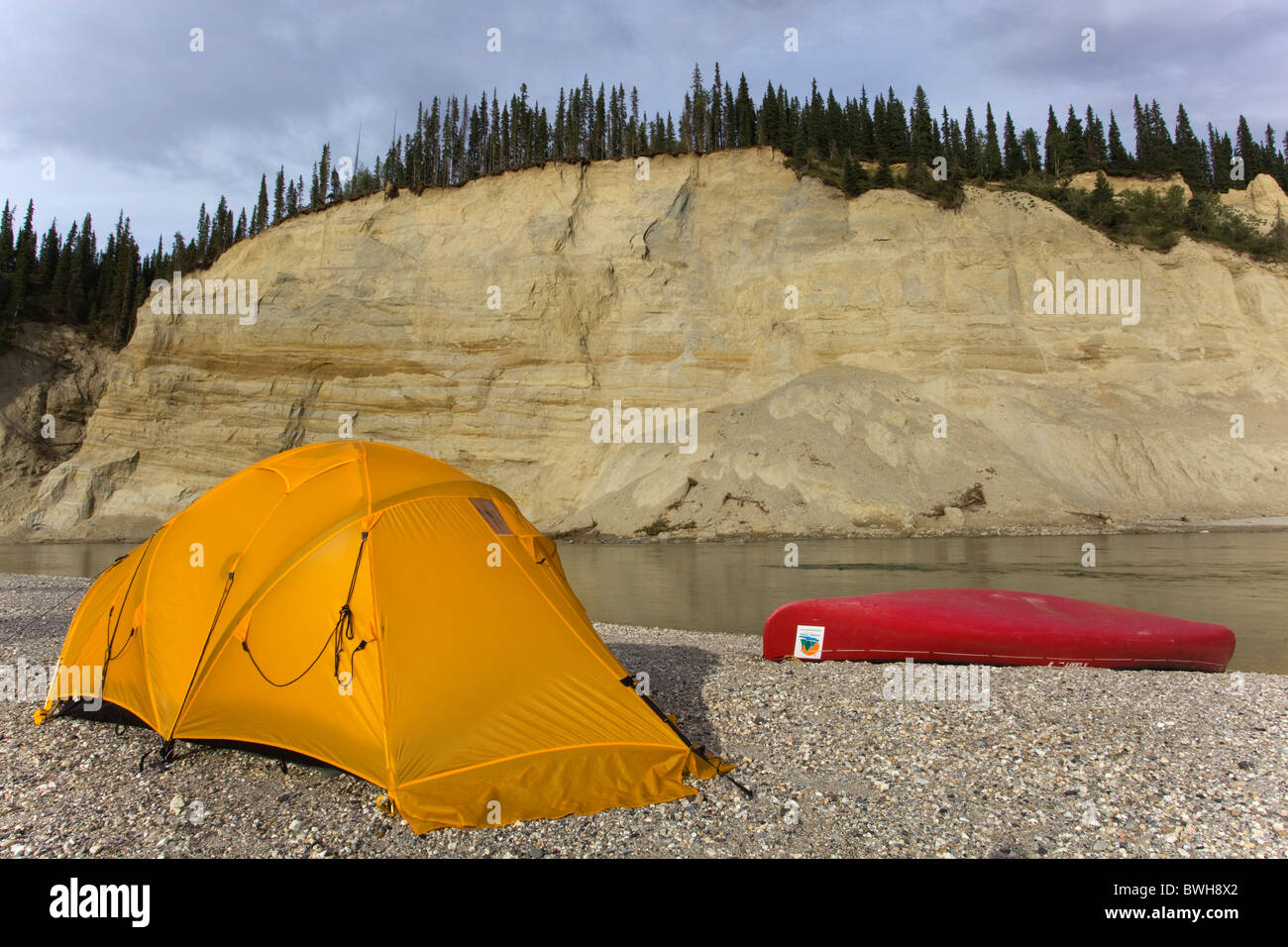 Camp, tent and canoe on a gravel bar, high cut bank, river cliff, erosion, behind, upper Liard River, Yukon Territory, Canada Stock Photo