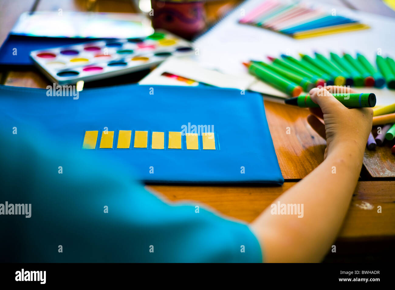 Young child holding a crayon about to write on his pencil case stationary paint pencils and crayons in background Stock Photo