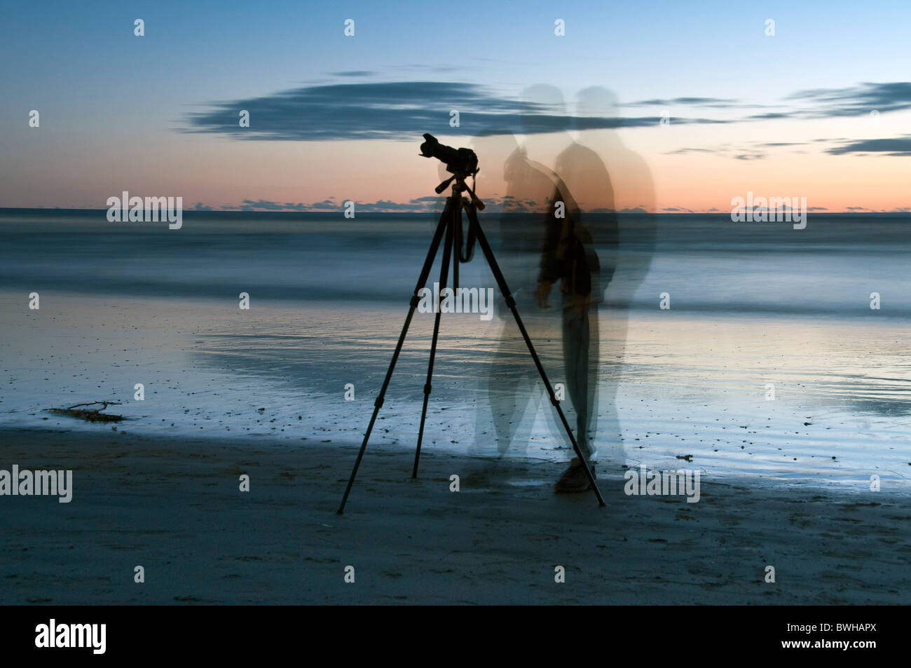 A photographer with a tripod at the ocean coast is blurred multiple ...