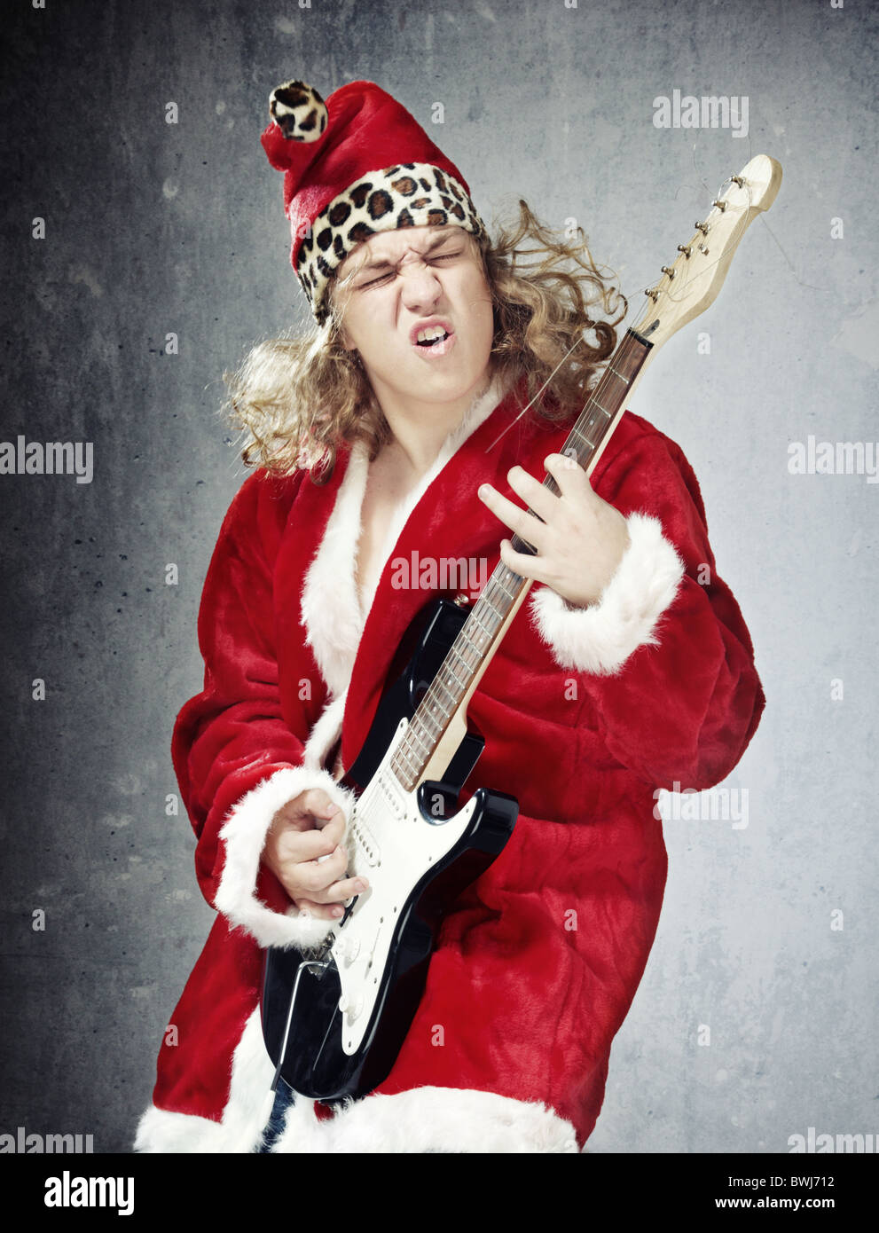 Man in the red and furry Santa Claus costume playing rock guitar on the grungy background Stock Photo