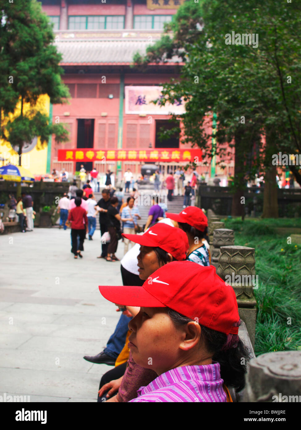 Chinese tourists wearing red hats wait on benches outside a temple in Hangzhou in the National Park Stock Photo