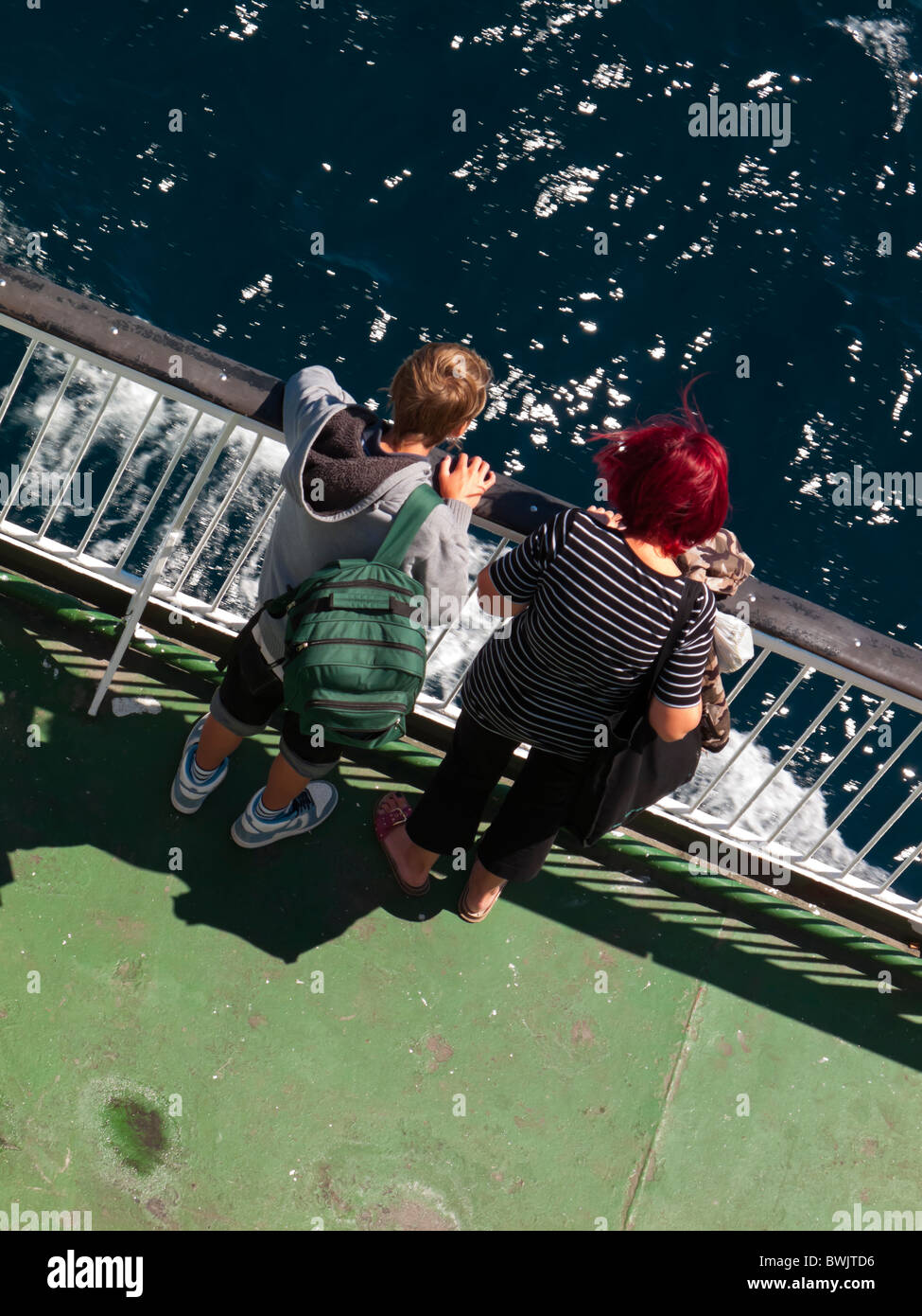 Two passengers looking down at the sea from the deck of a ship with the water visible below Stock Photo