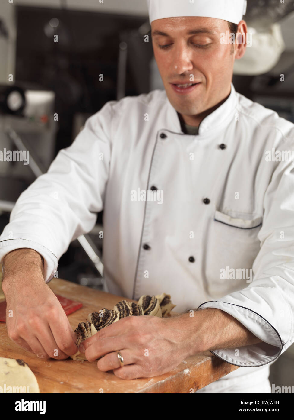 Portrait of a baker making pastries in a bakery. The focus is on the pastry. Stock Photo