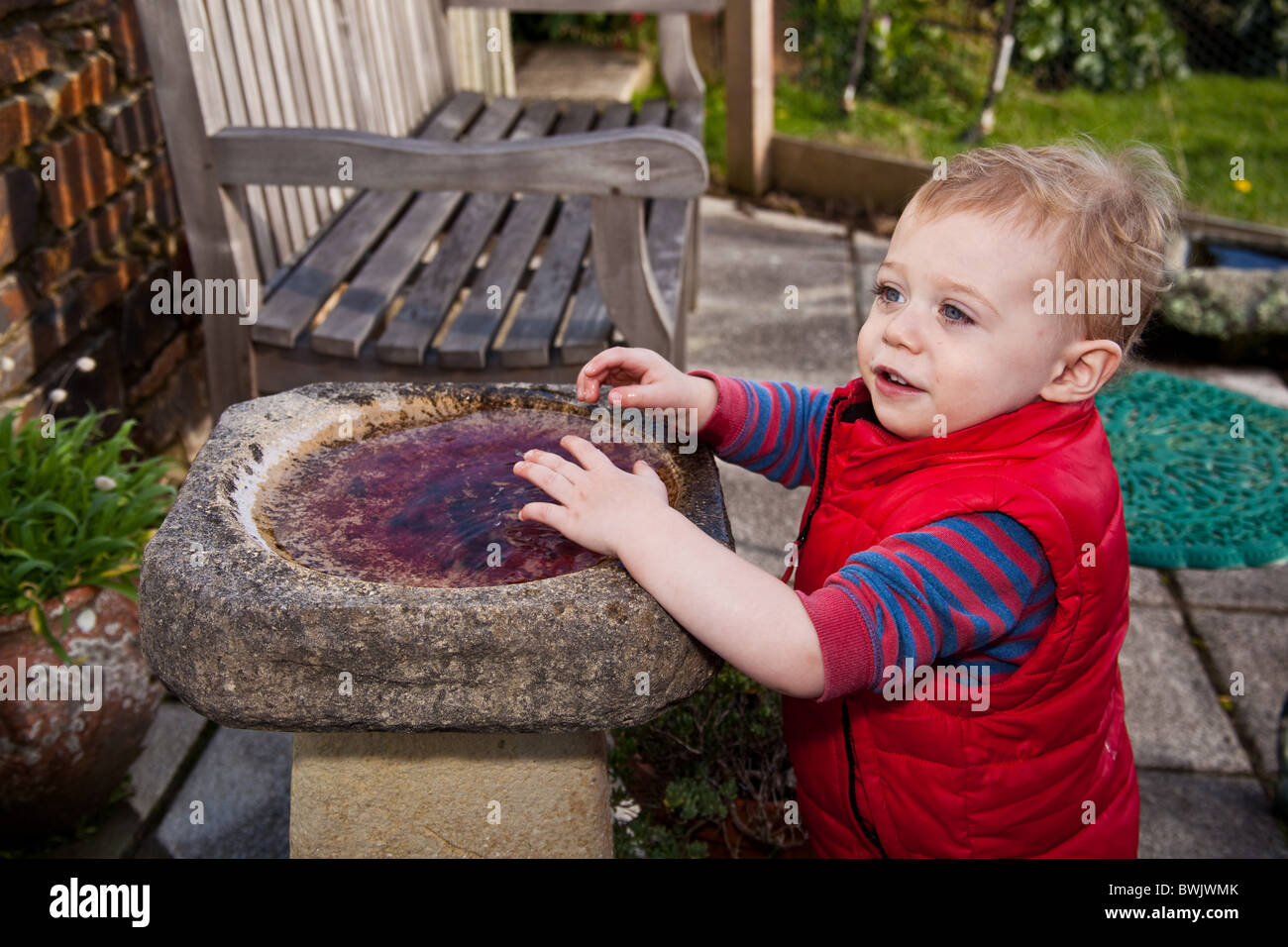 One year old baby boy playing with a bird bath, St Mawes, Cornwall