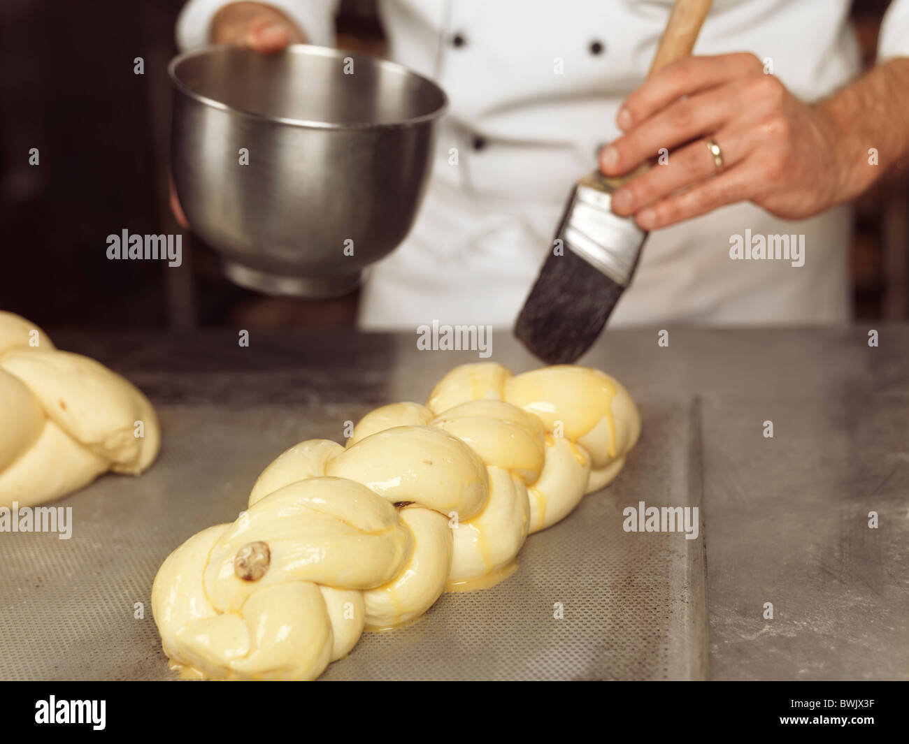 Baker brushing egg yolk glazing on raw braided sweet bread Stock Photo