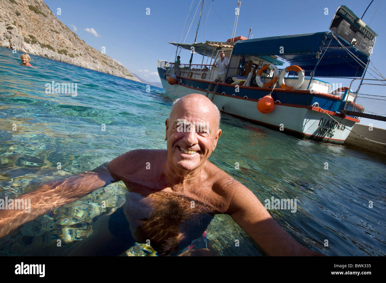 Fit, healthy, tanned older man smiling at camera as he swims in the sea off the Greek Island of Symi Stock Photo