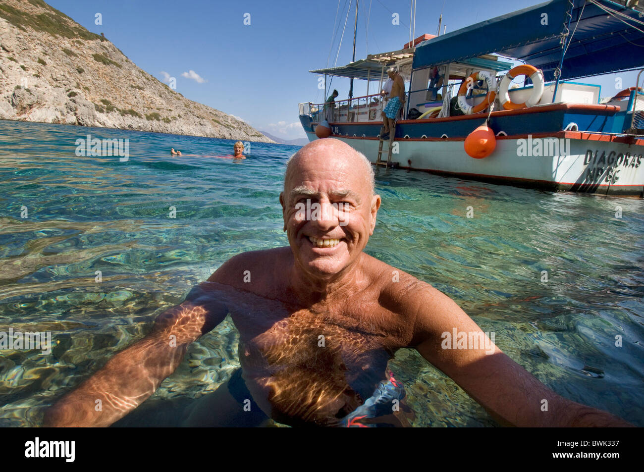 Fit, healthy, tanned older man smiling at camera as he swims in the sea off the Greek Island of Symi Stock Photo