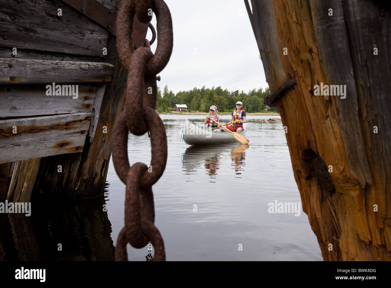 A girl and a woman in a canoe between ship wrecks on the island of Norrbyskaer, Vaesterbotten, Sweden, Europe Stock Photo