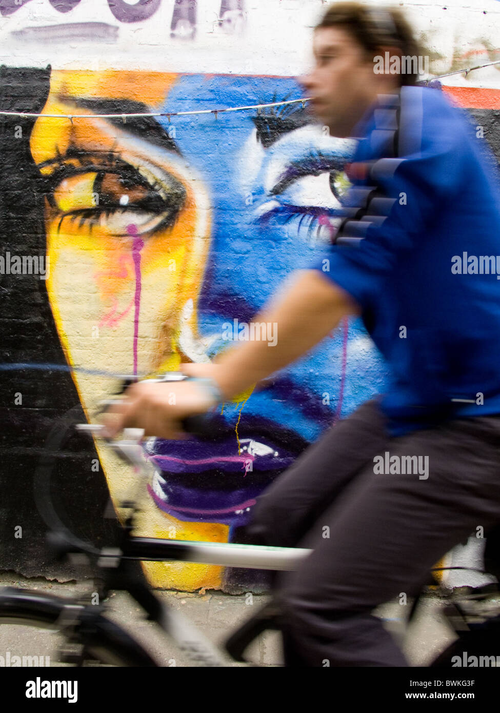 A cyclist passes a large graffiti face that appears to be watching him Stock Photo