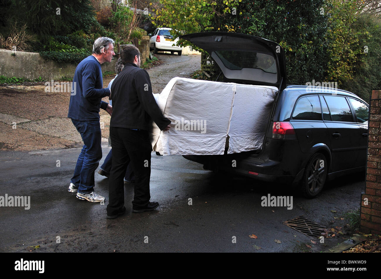 Two men attempting to load a sofa into a car, without success Stock Photo