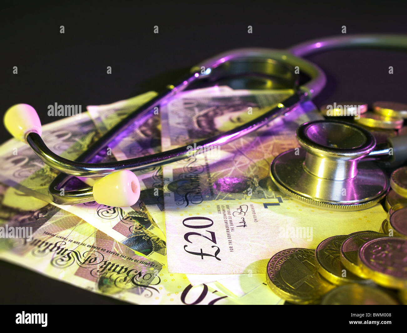 British pound coins stacked in background on a bed of twenty pound notes with a stethoscope Stock Photo
