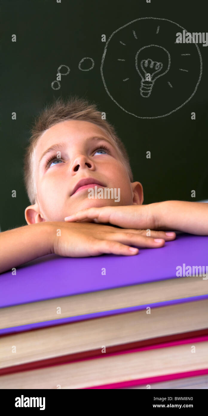 Face of diligent schoolboy looking upwards with his head on stack of books over black background Stock Photo