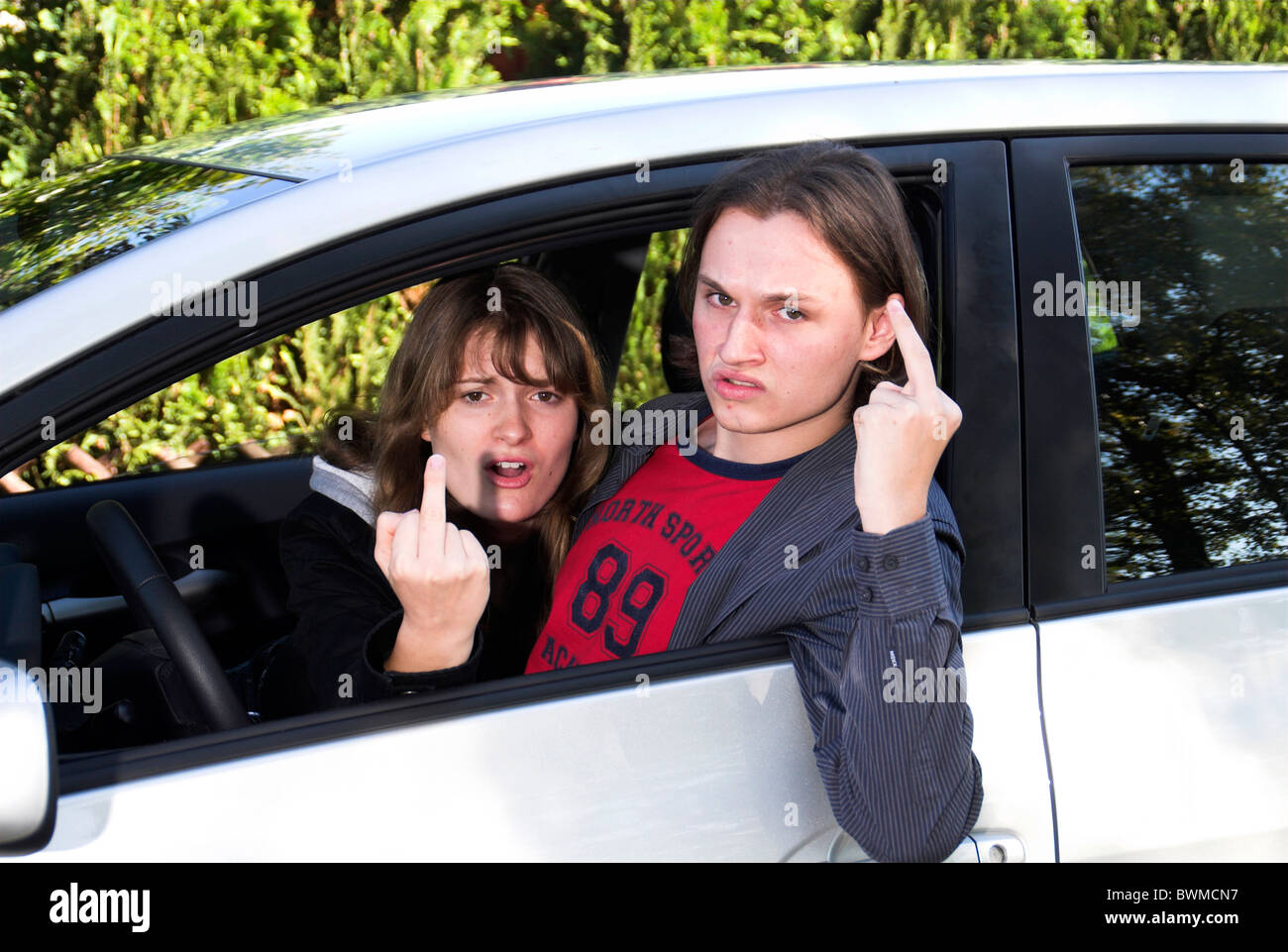 Road conflict. Woman showing middle finger and jeering someone outside her  car. Photos