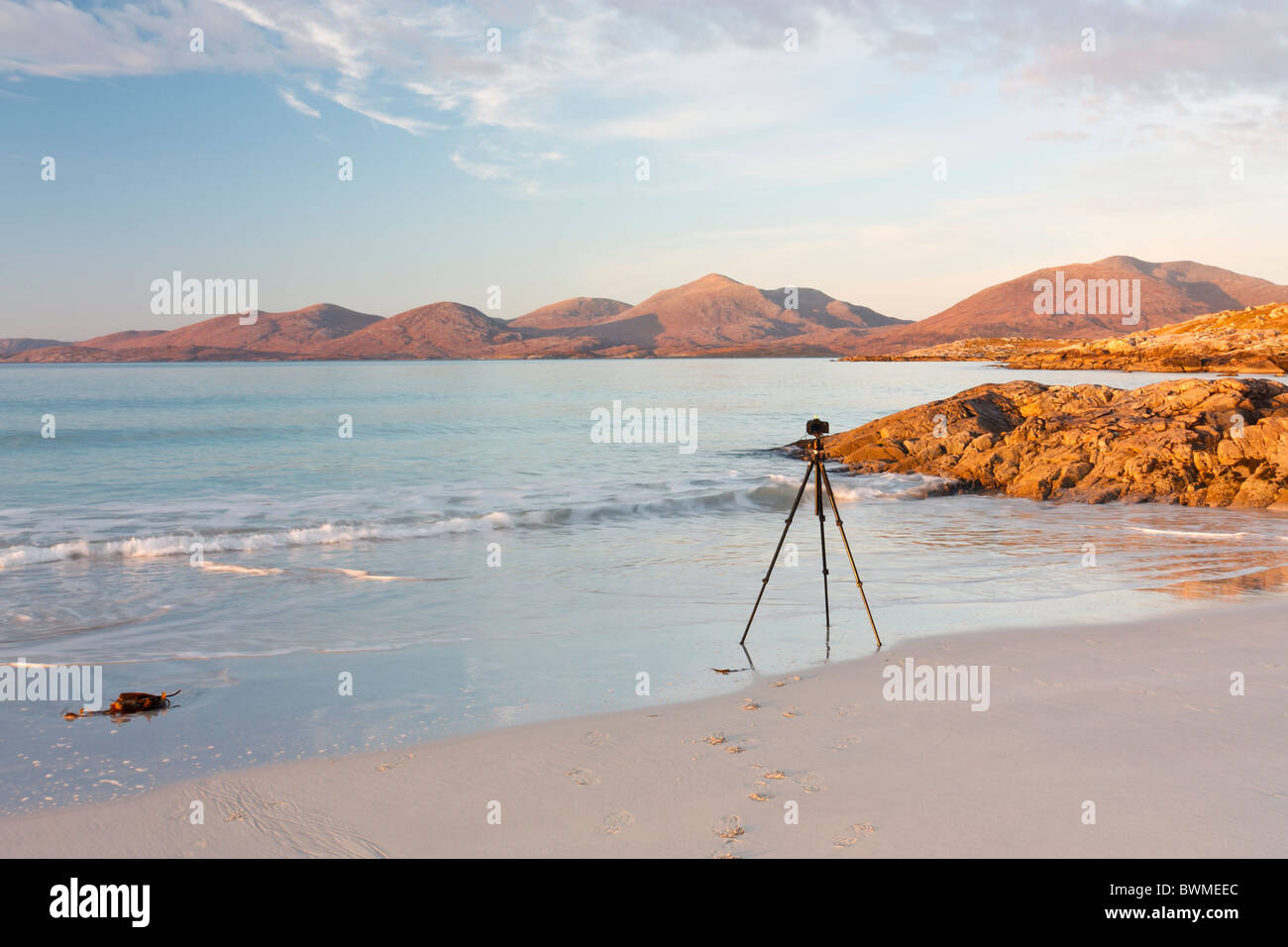A photographers tripod stands where the sand meets the sea ready to capture the perfect shot in golden light Stock Photo
