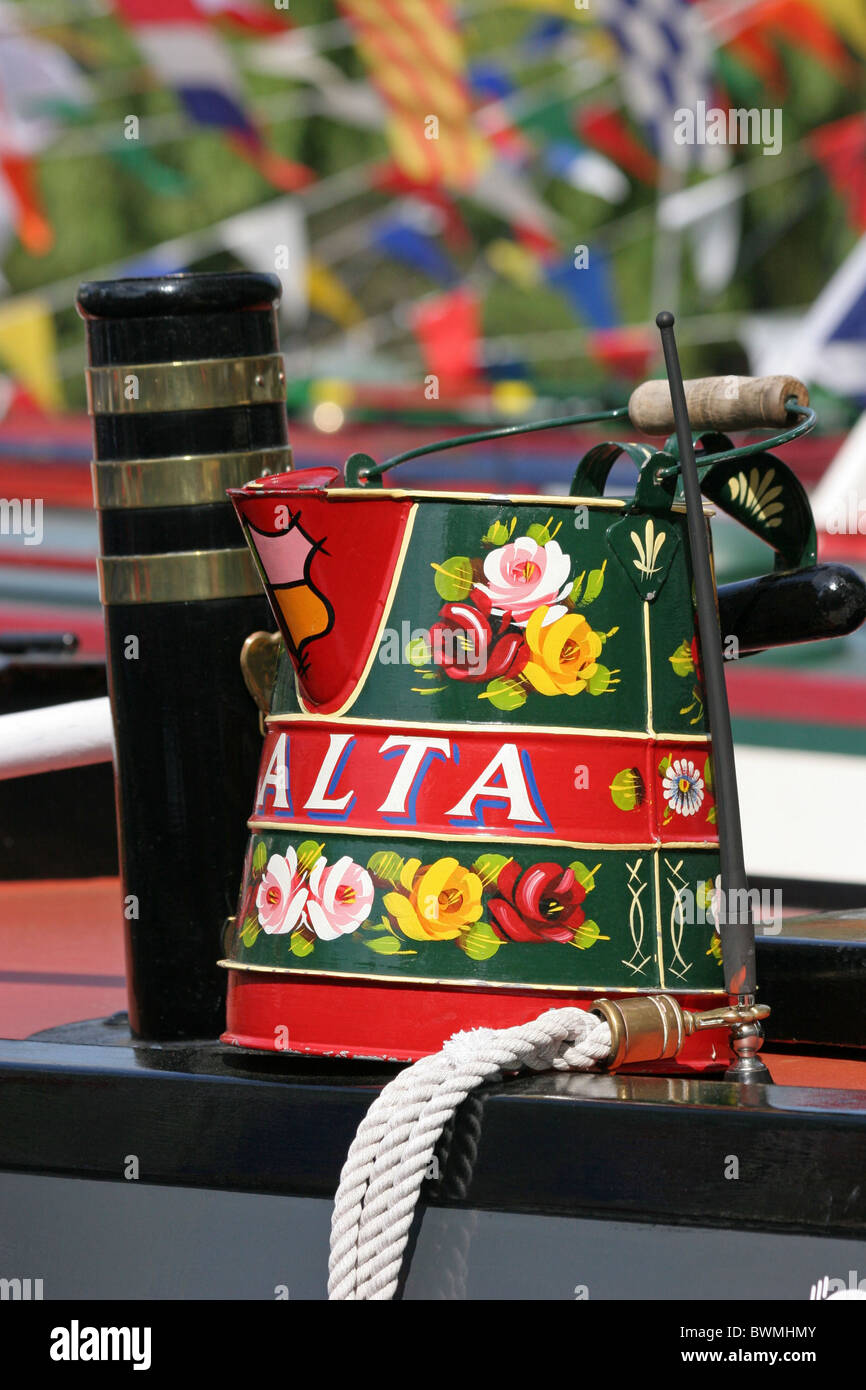 a decorated buckby can traditionaly painted with castles and roses next tto a black and brass chimney on a narrowboat Stock Photo