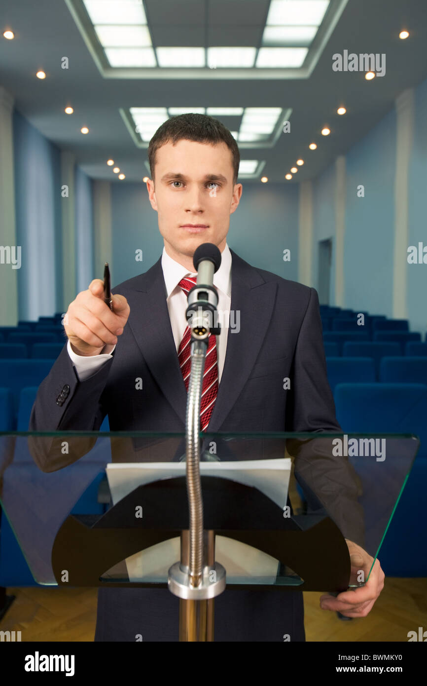 Portrait of lecturer with rows of armchairs behind in conference hall