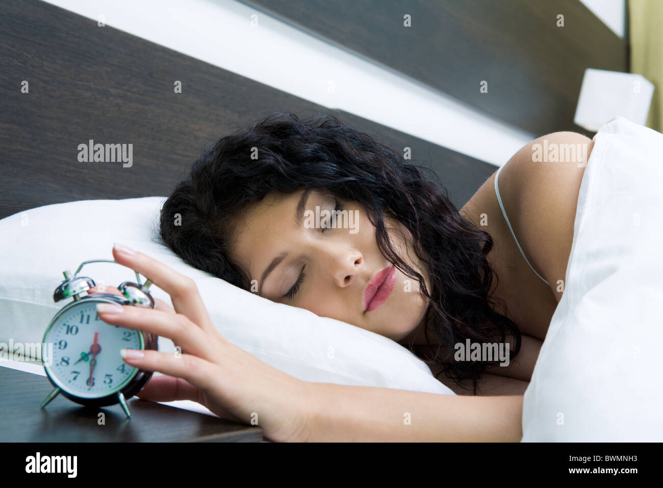 Image of female keeping her hand on top of alarm clock after awakening in the morning Stock Photo