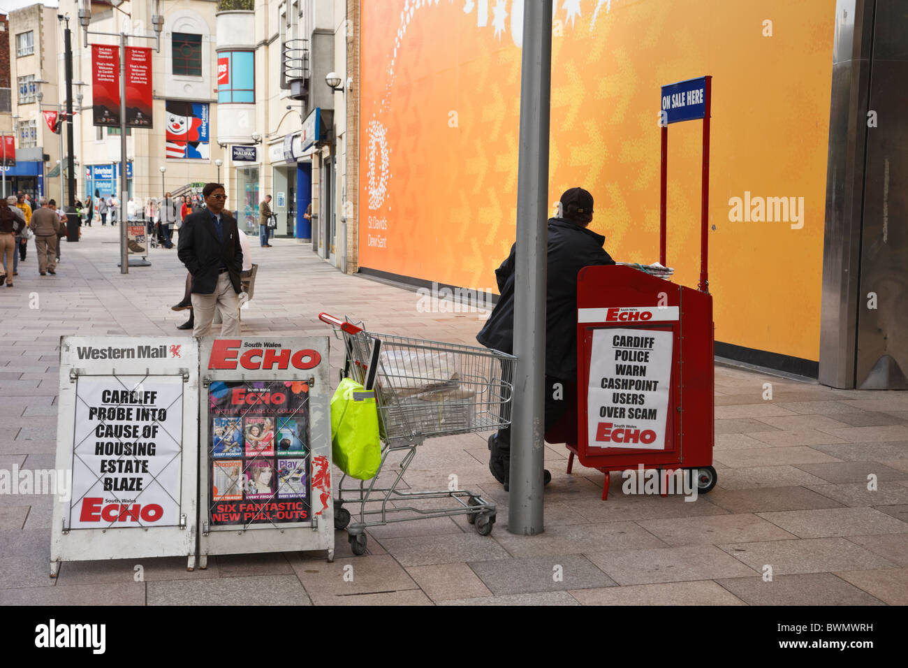 Street vender selling local newspapers from a newspaper stand in the city centre. Cardiff, Glamorgan, South Wales, UK Stock Photo