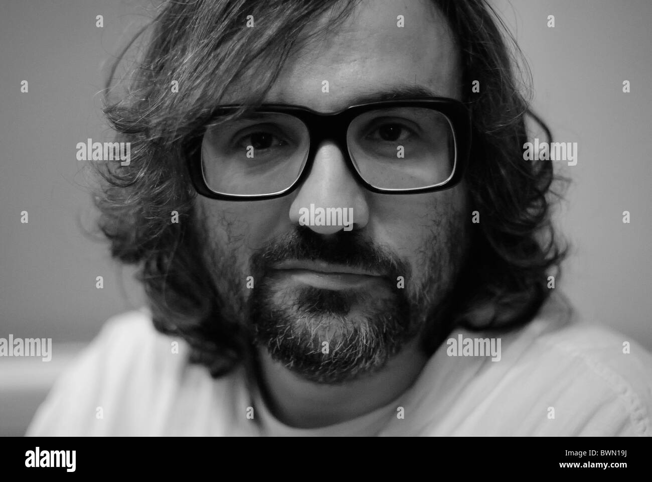 A black and white photo of a bearded man wearing thick-rimmed 1970s-style glasses. Stock Photo