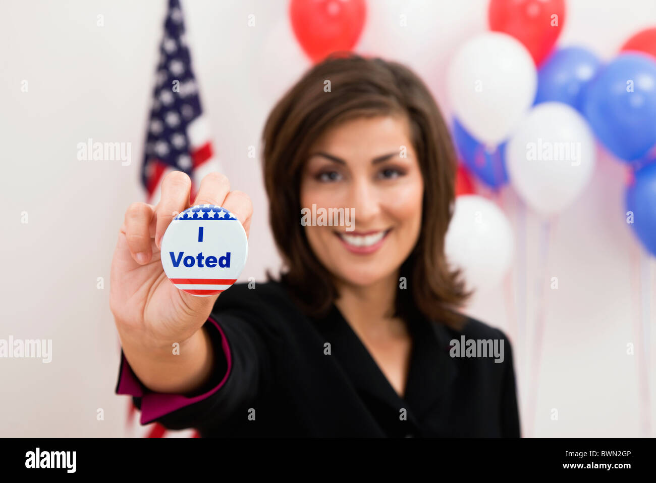 USA, Illinois, Metamora, Portrait of smiling woman holding vote button, US flag and balloons in background Stock Photo