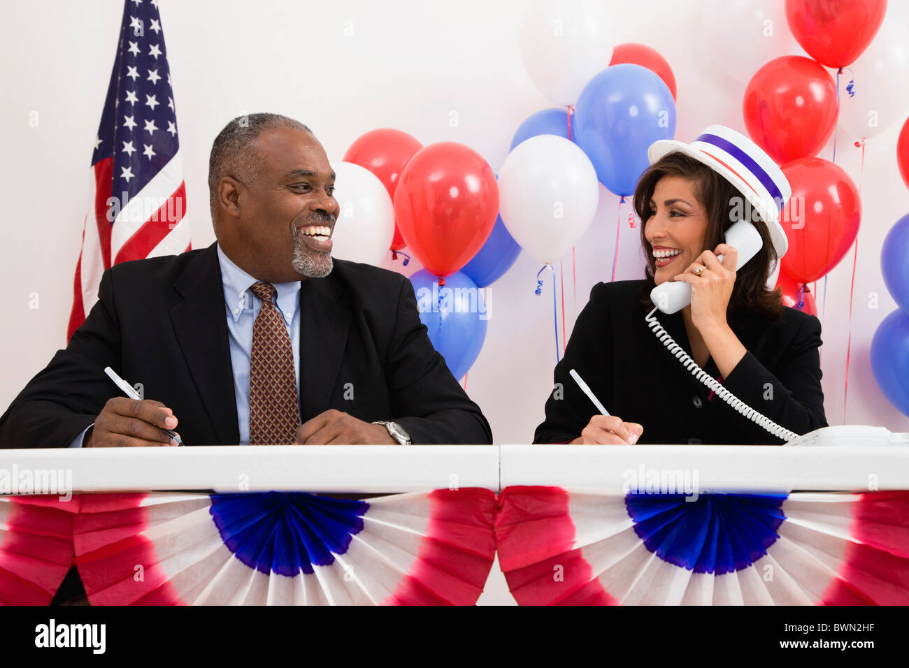 USA, Illinois, Metamora, Smiling man and woman at polling place table, red and blue balloons in background Stock Photo
