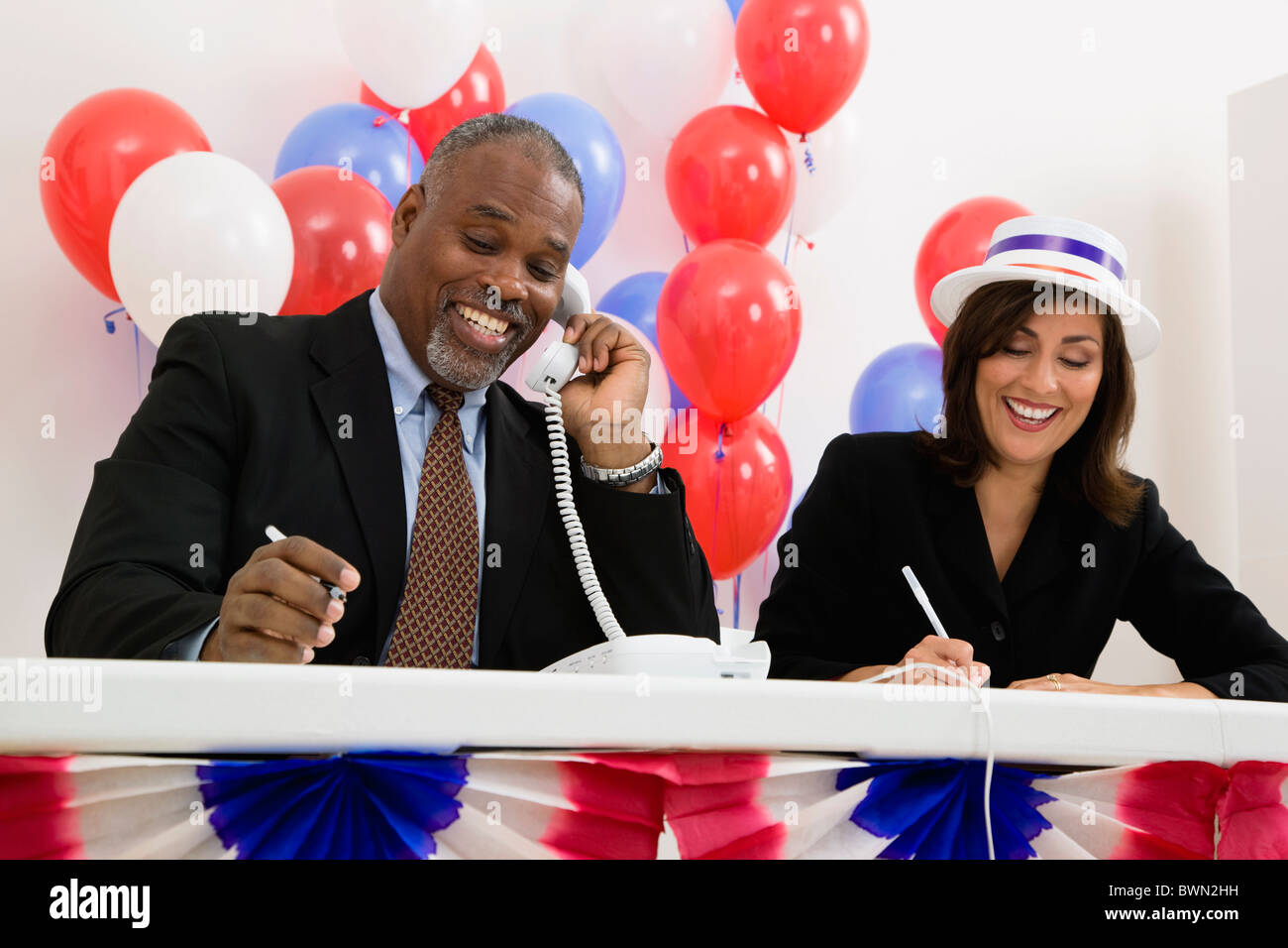 USA, Illinois, Metamora, Smiling man and woman at polling place table, red and blue balloons in background Stock Photo