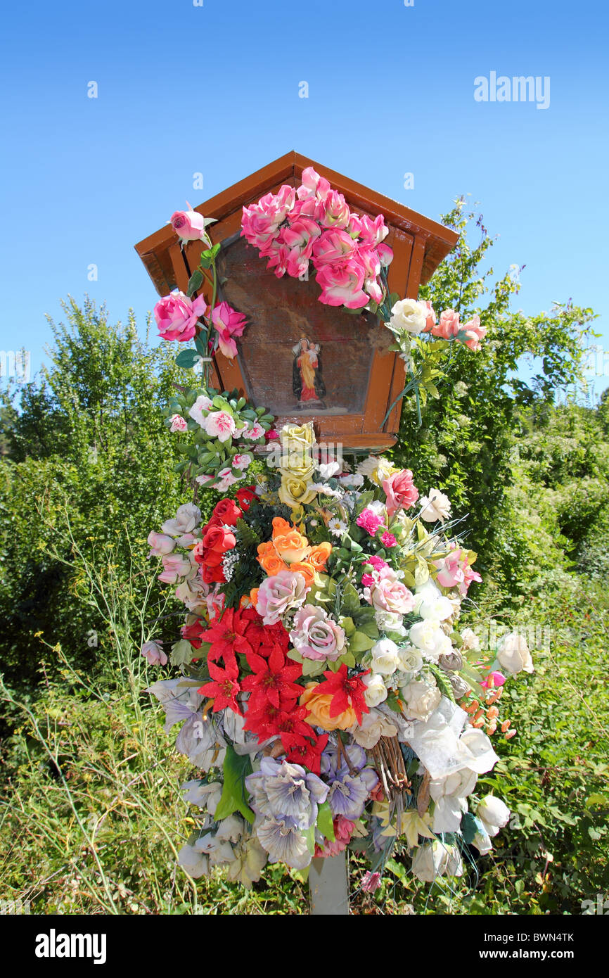 Virgin Christian Catholic religion sacred icon figurine with flowers outdoor Stock Photo