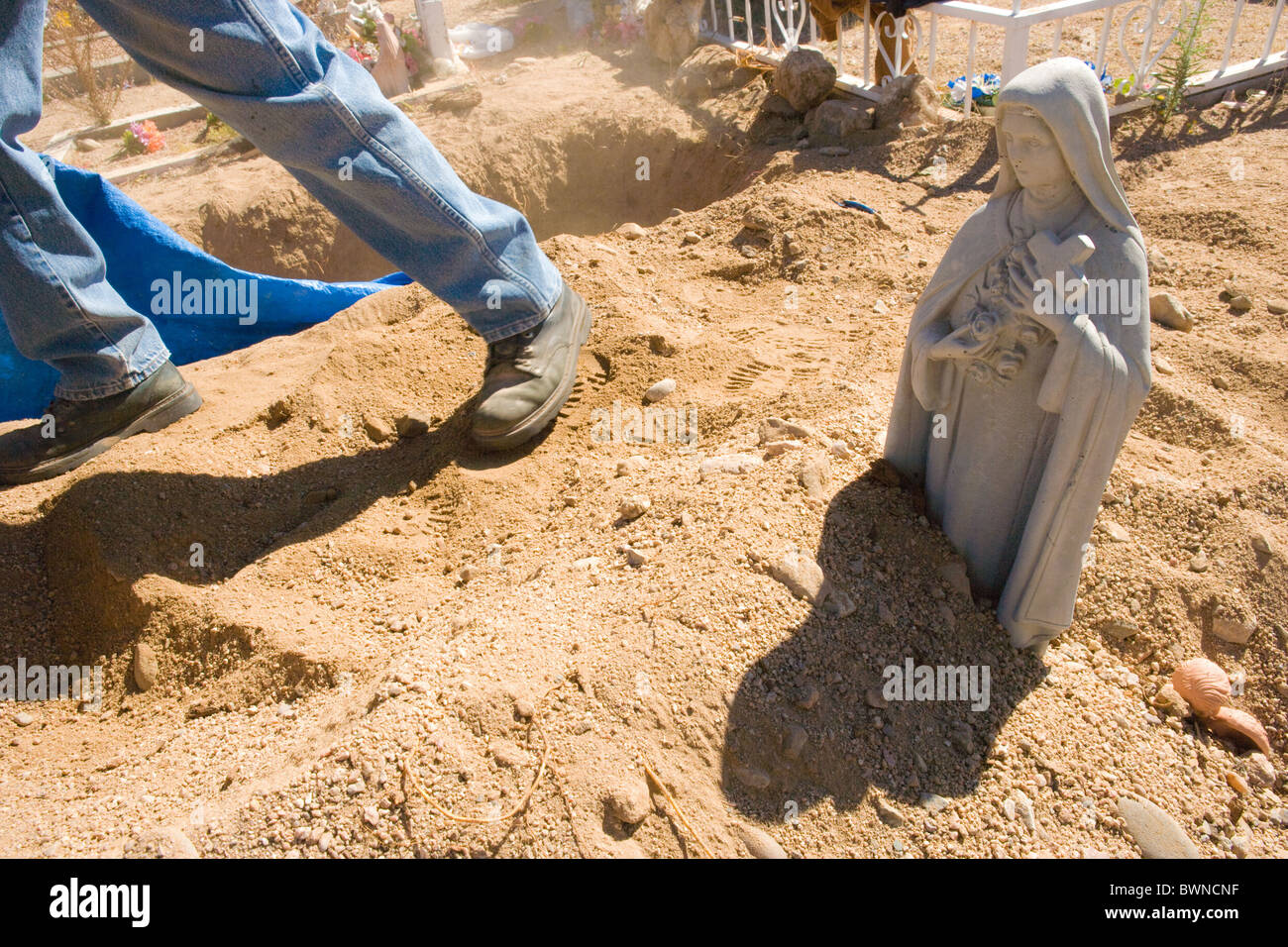 Man digging a grave, dirt covering base of Mother Mary statue, cemetery, USA Stock Photo