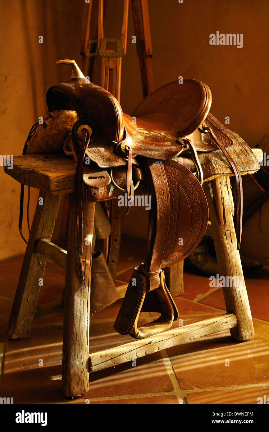 Authentic western cowboy leather saddle sitting on rustic wooden bench with light flowing in from window outside of frame. Stock Photo