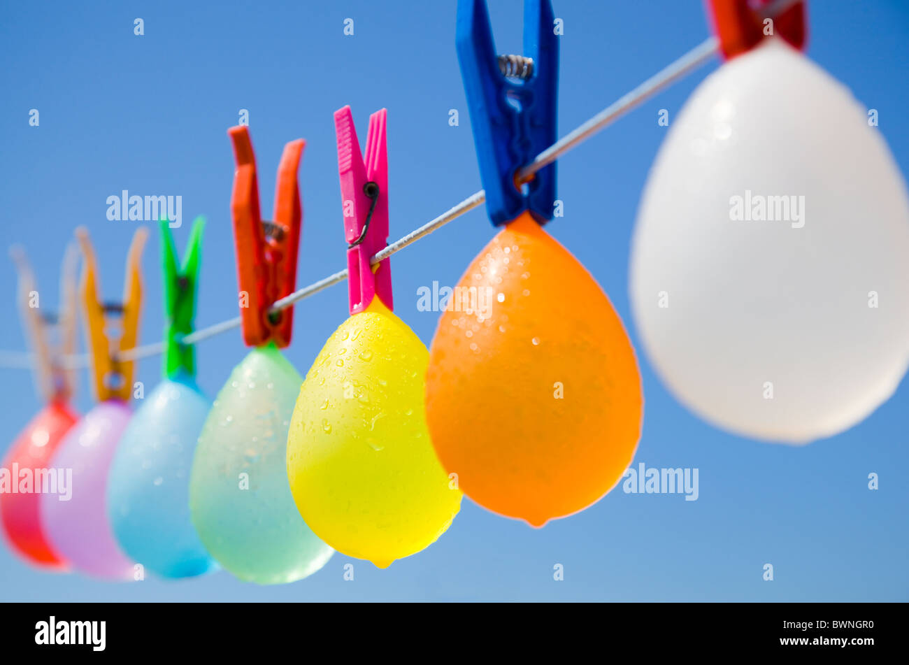 Selective view of a colored bunch of balloons with water-drops hanging on a clothesline with a blue sky as background Stock Photo