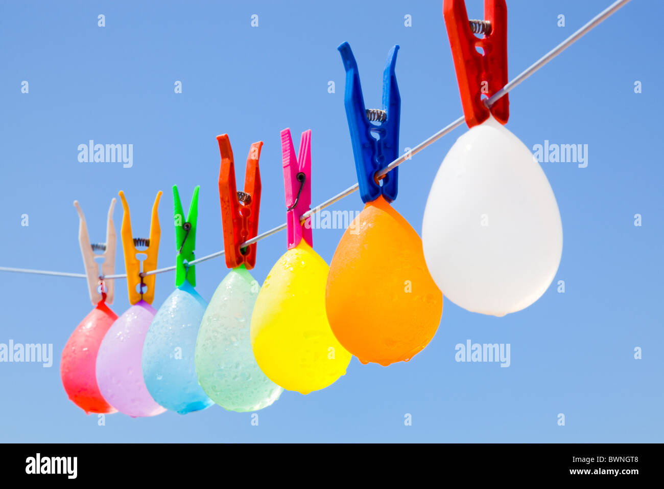 Selective focus on a colored bunch of balloons with water-drops hanging on a clothesline with a blue sky as background Stock Photo