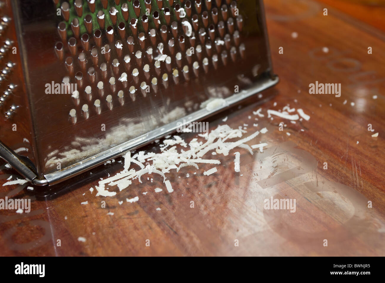 Slivers of grated Parmesan cheese next to worn cheese grater. Stock Photo