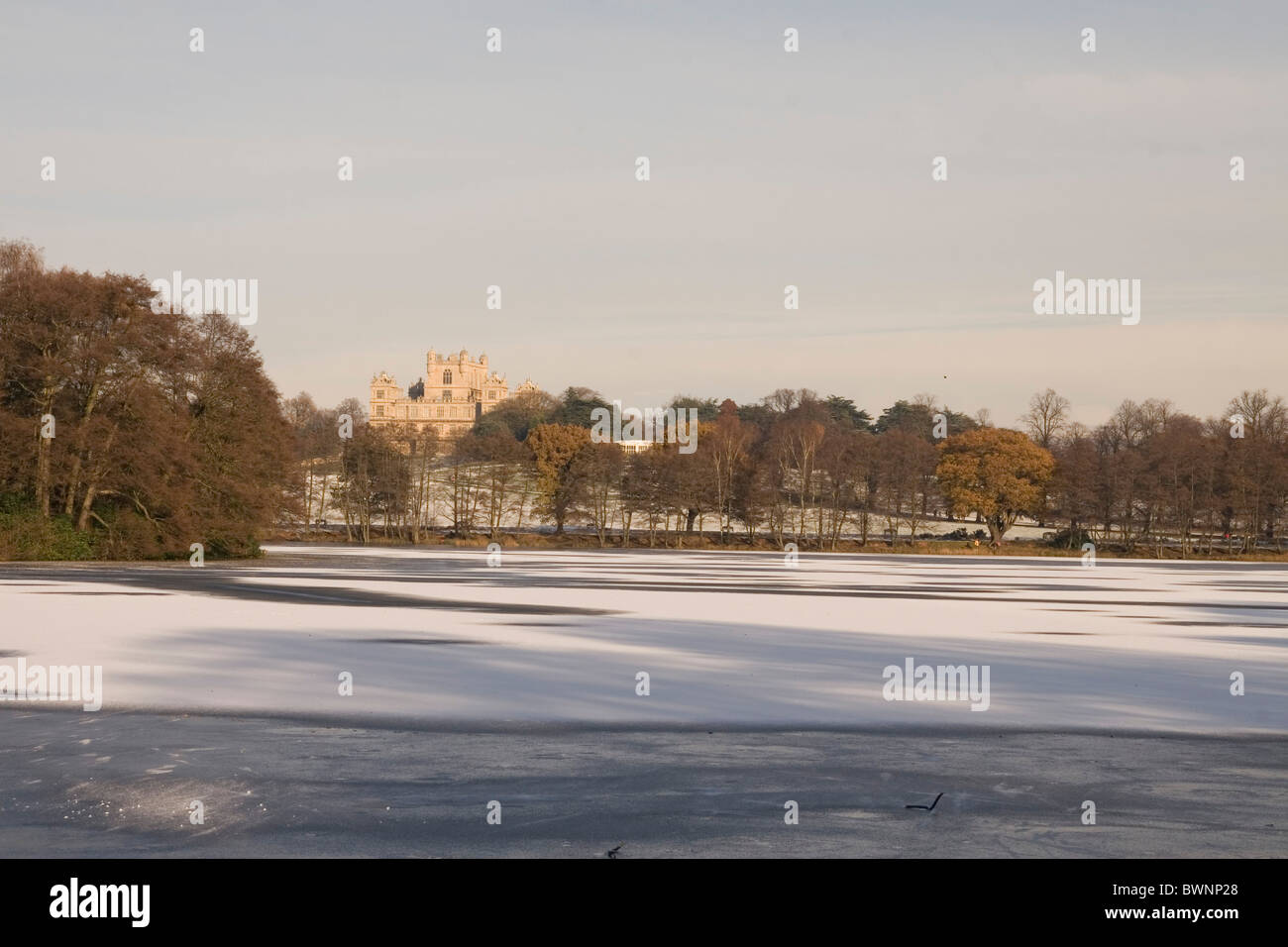 Wollaton Hall pictured from across the lake, which is frozen and has a ...