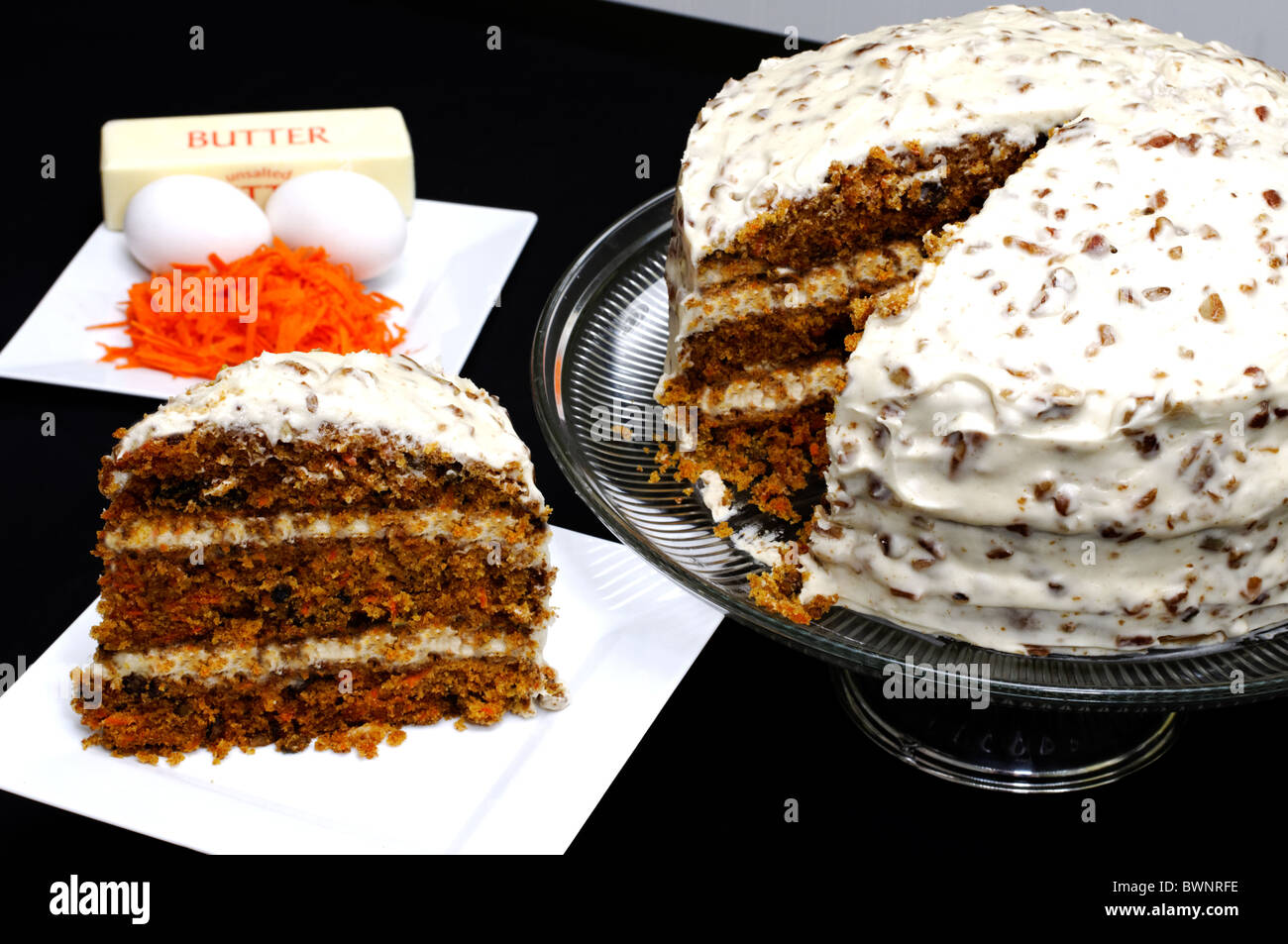 Slice of carrot cake, stick of butter, shredded carrots, and fresh eggs with whole carrot cake. Stock Photo
