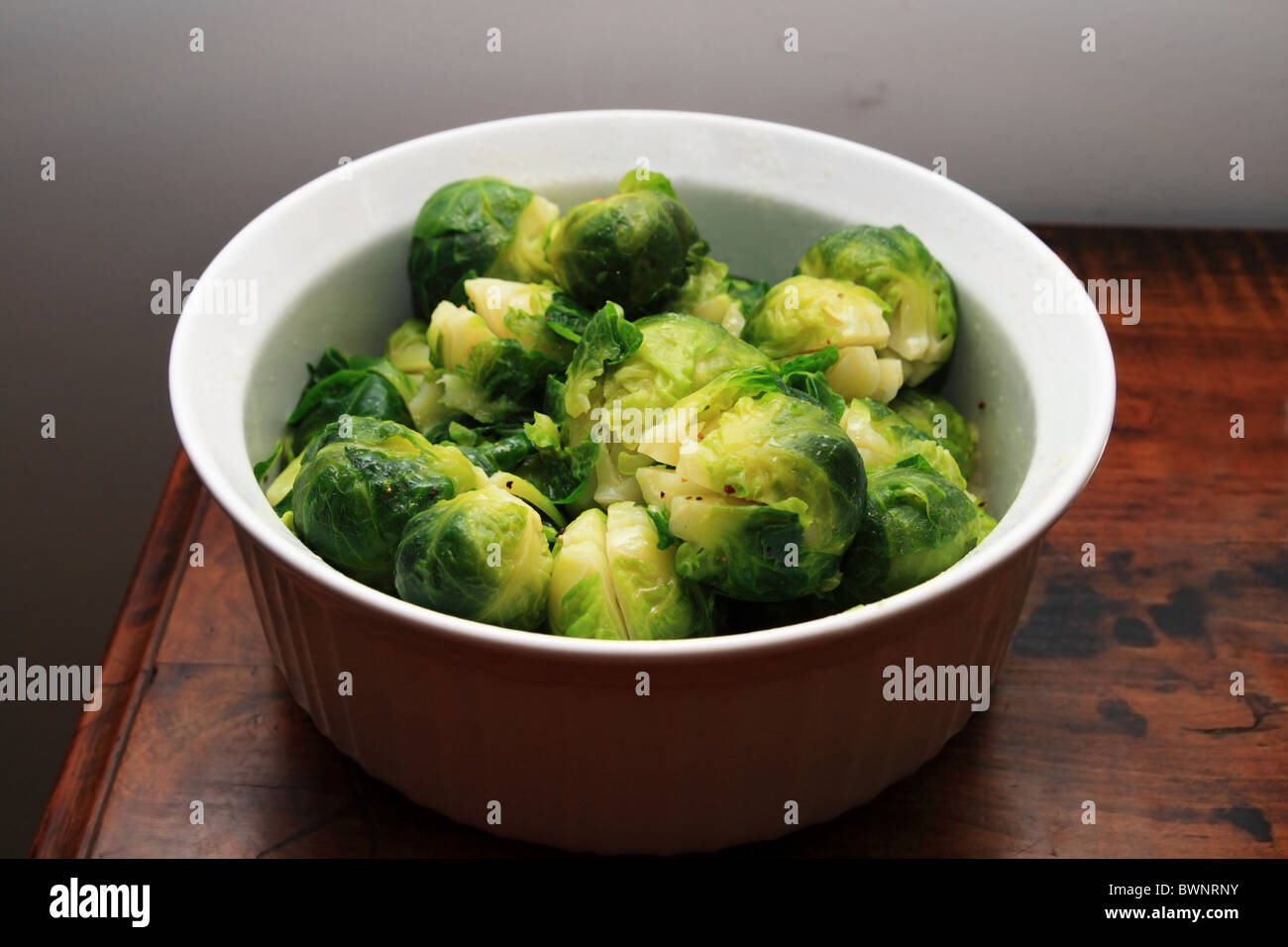 white bowl of cooked brussel sprouts on the end of a wooden table Stock Photo