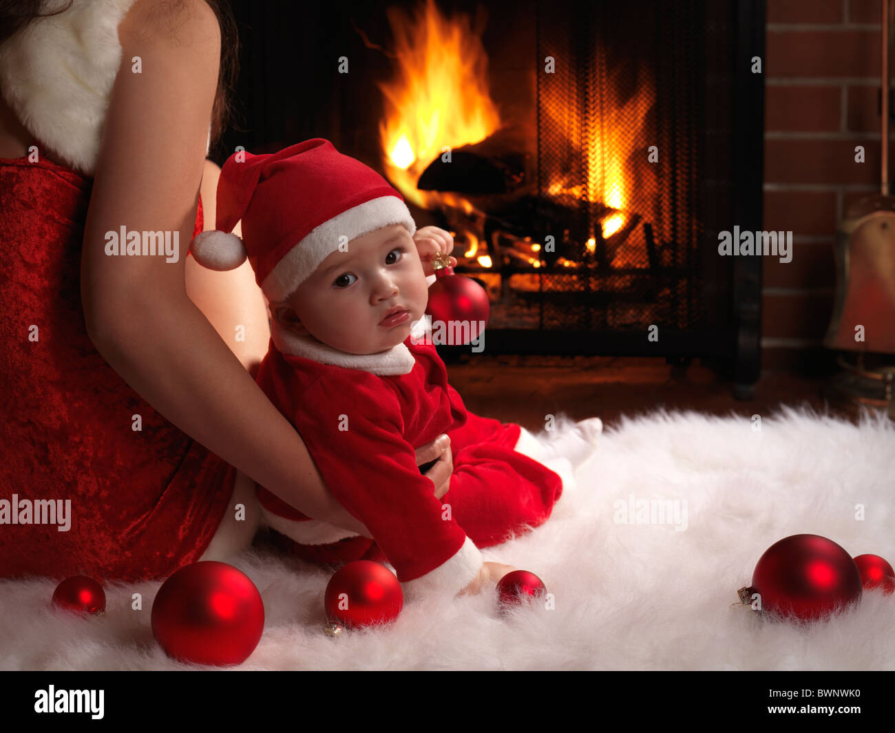 Mother and a little baby boy sitting in front of a fireplace in Christmas costumes. Stock Photo