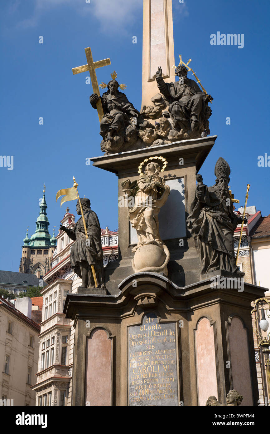 Prague - baroque column of Holy Trinity and tower of st. Vitus cathedral - infront of St Nicolas Church at Lesser Town Square - Stock Photo