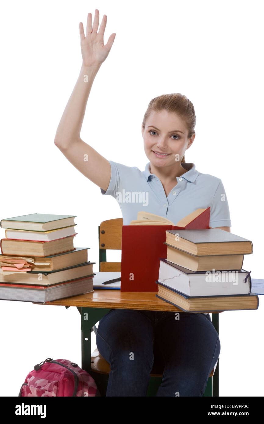 High school or college female student sitting by the desk with books raising her arm signaling that she know and ready to answer Stock Photo