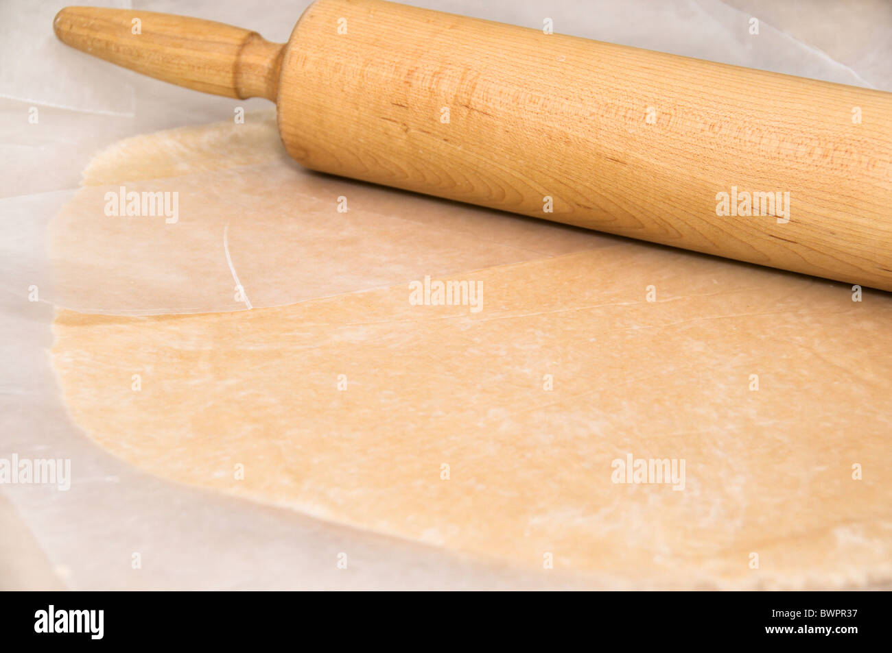 Pie pastry crust is conveniently flattened with a rolling pin between sheets of waxed paper to eliminate a sticky mess. Stock Photo