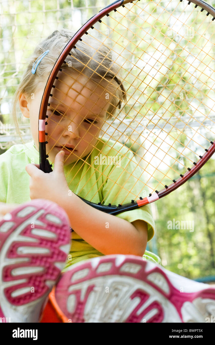 Sad child with tennis racket looking through its net outdoors during ...