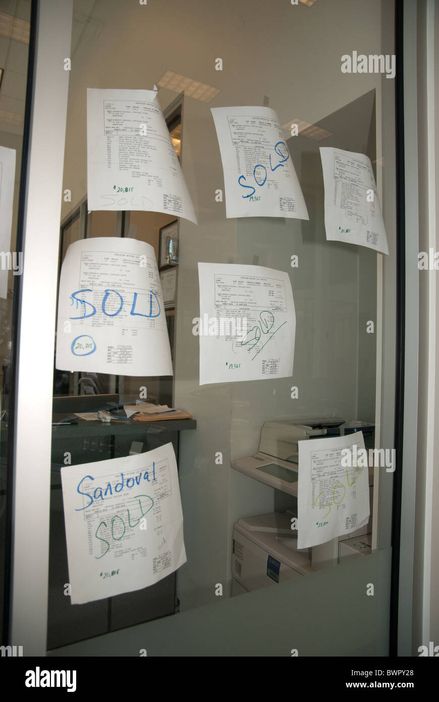 Paperwork marked "Sold" on window of sales office at car dealership