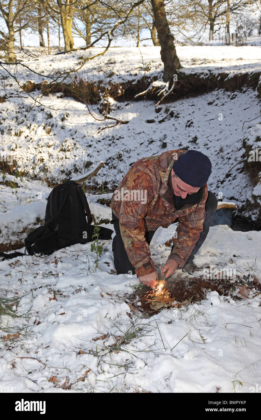 Using a Fire Steel and Birch Bark to Create Fire in a Woodland Environment in Winter Snow United Kingdom Stock Photo