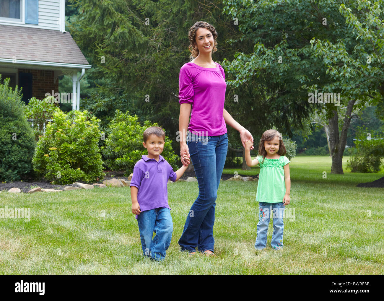 Mother holding hands with son and daughter in front yard Stock Photo