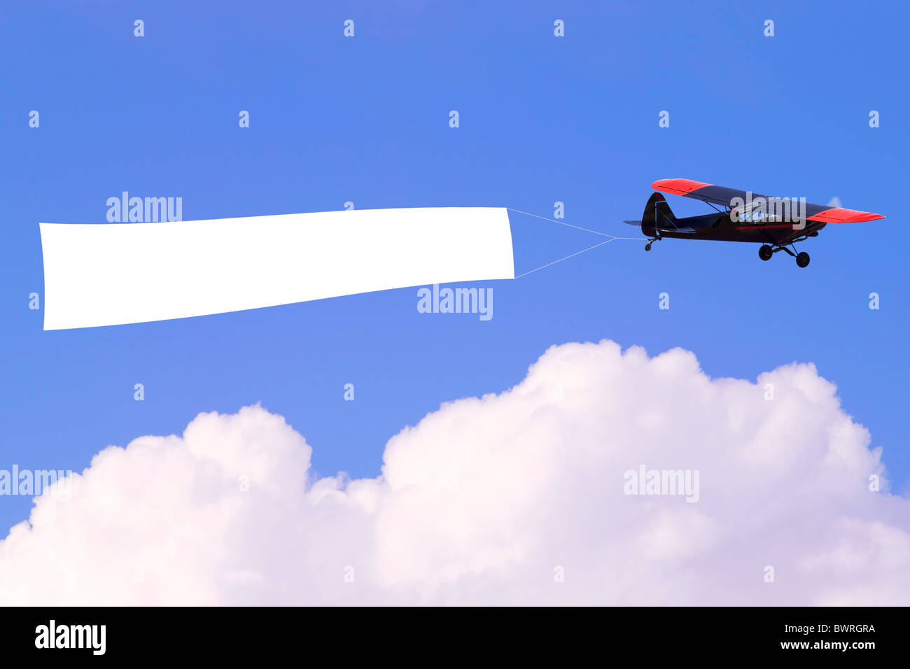 An airplane flying through the sky pulling a blank white banner to add your own message. Stock Photo