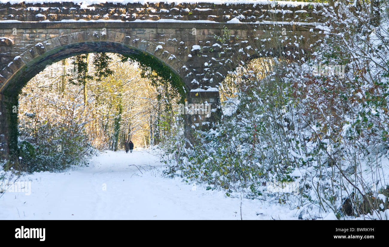 Distant walking couple taking  a walk alone a disused rail line now used as  a footpath after a snow fall. Stock Photo