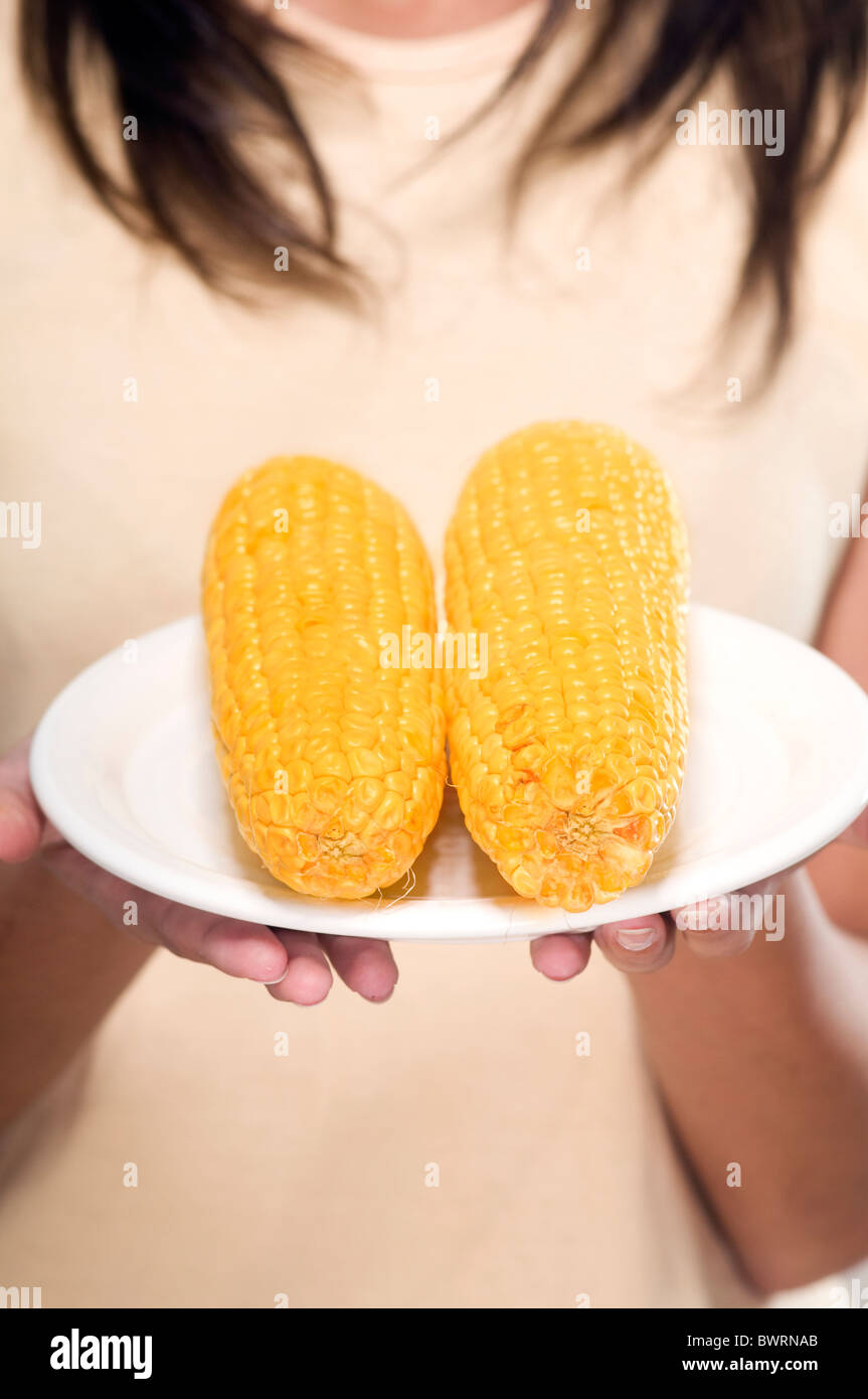Young woman holding a plate with two corns Stock Photo