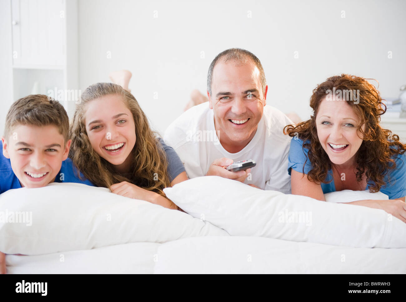 Laughing Hispanic family laying on bed together Stock Photo